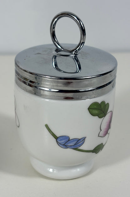 A white ceramic container with a shiny silver metal lid featuring a loop handle, decorated with a blue flower and green leaves on the front.