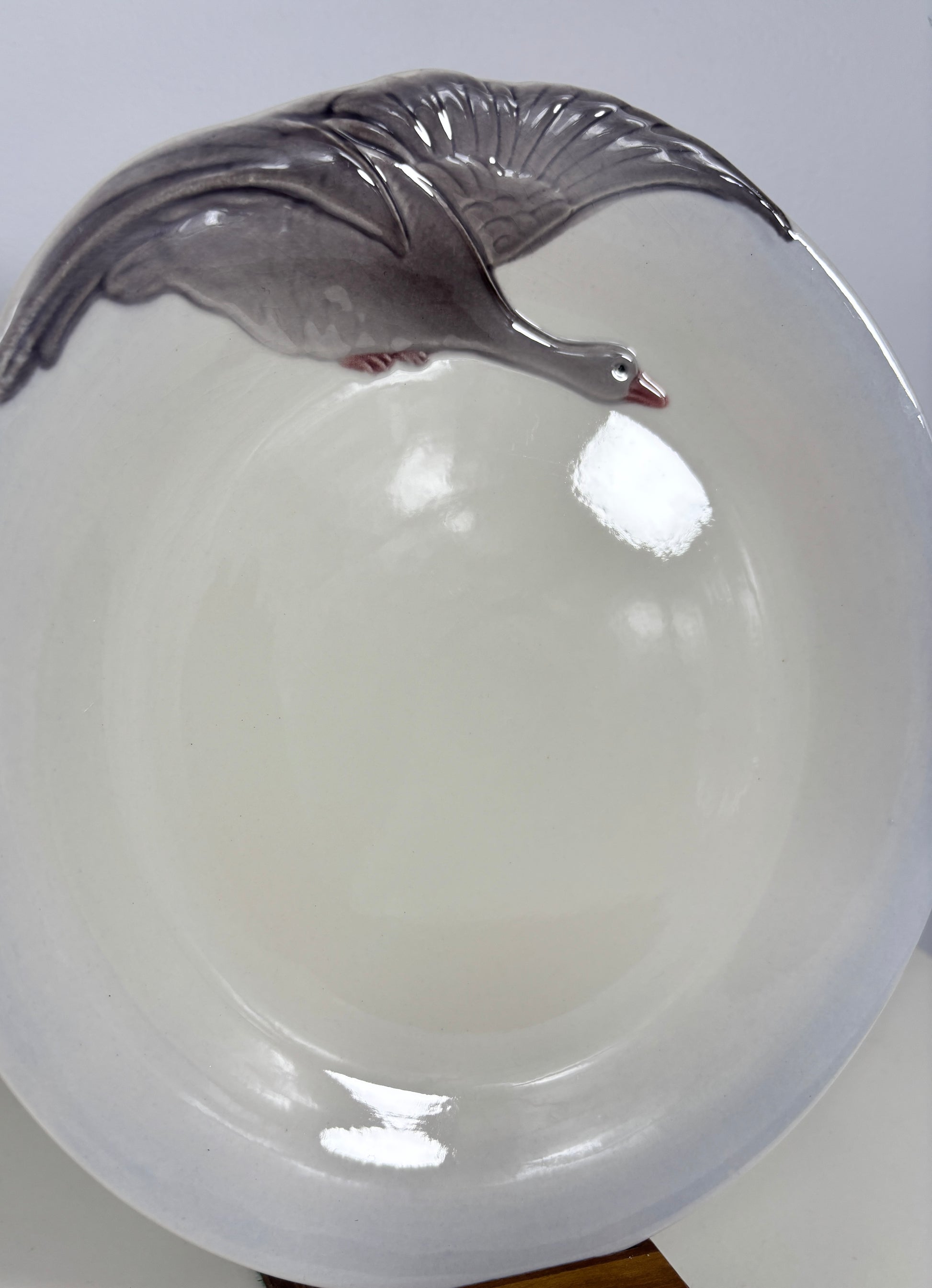 A white ceramic bowl featuring a raised gray goose design along the rim, shown against a plain light background.