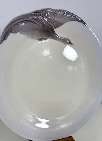 A white ceramic bowl featuring a raised gray goose design along the rim, shown against a plain light background.