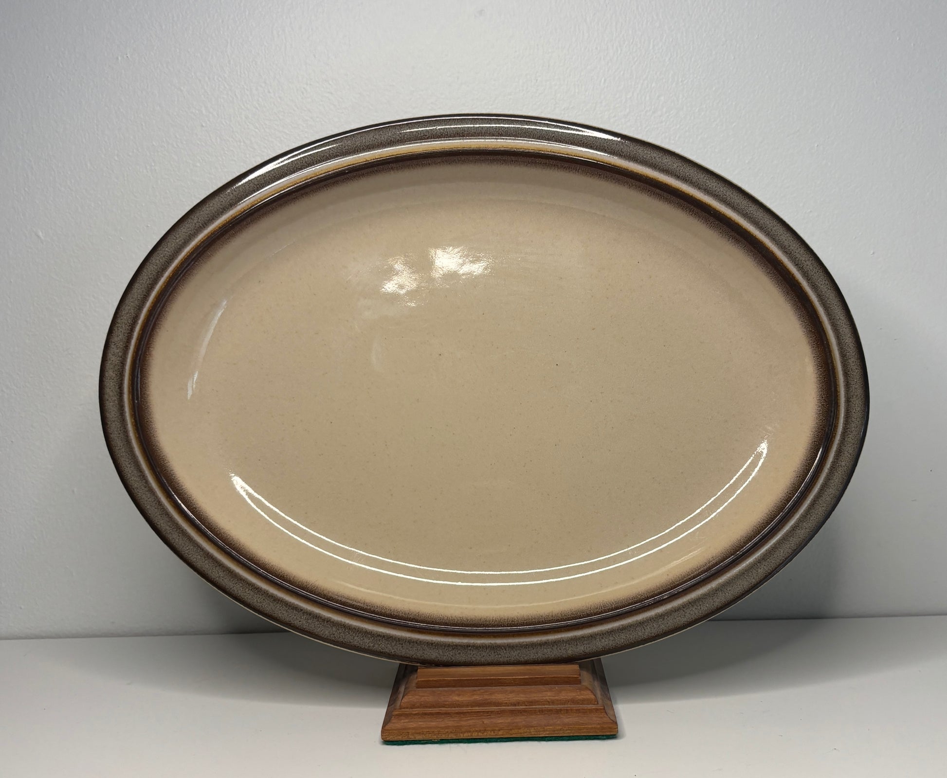 Oval ceramic platter with brown rim on a stand against a white background