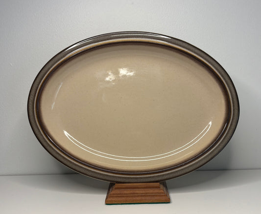 Oval ceramic platter with brown rim on a stand against a white background