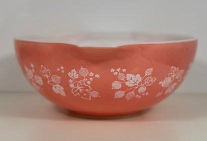 A coral orange glass bowl with a white floral and berry pattern, photographed against a neutral light gray background.