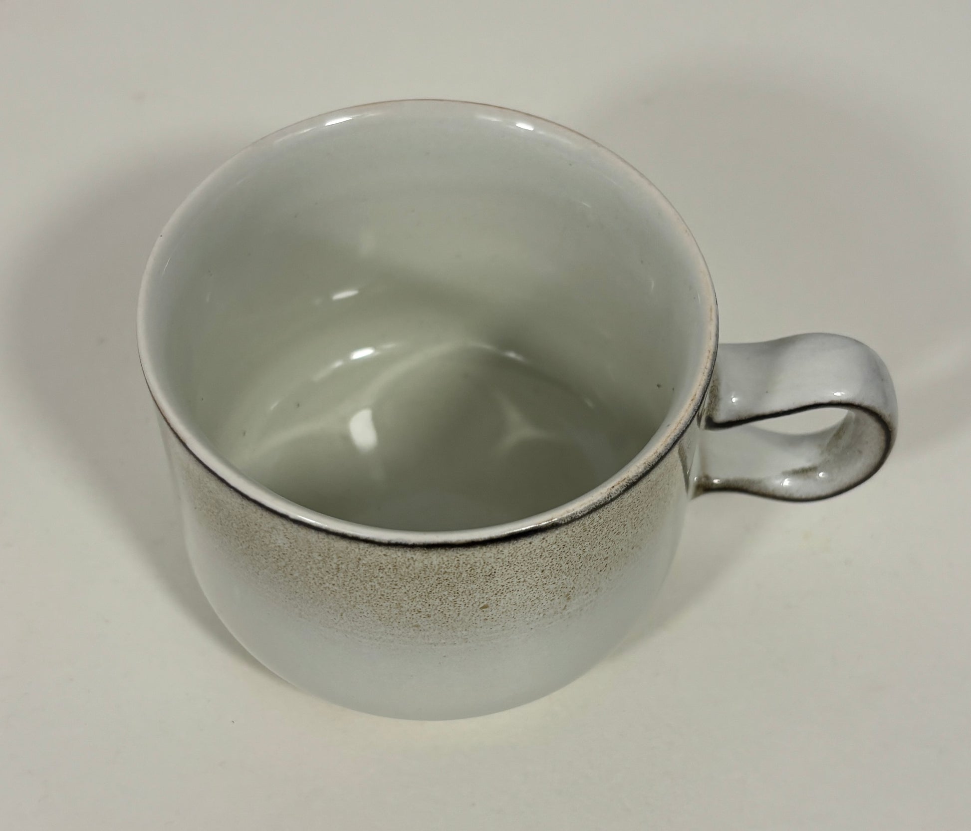 A ceramic coffee mug with a speckled gray exterior and a glossy off-white interior, featuring a curved handle.