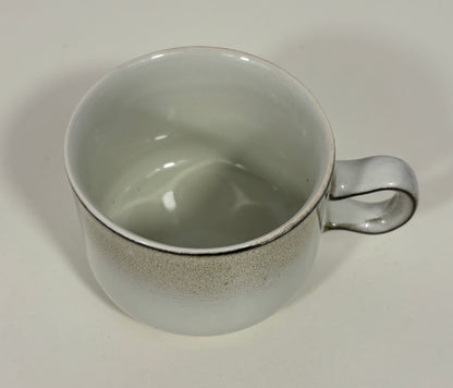 A ceramic coffee mug with a speckled gray exterior and a glossy off-white interior, featuring a curved handle.