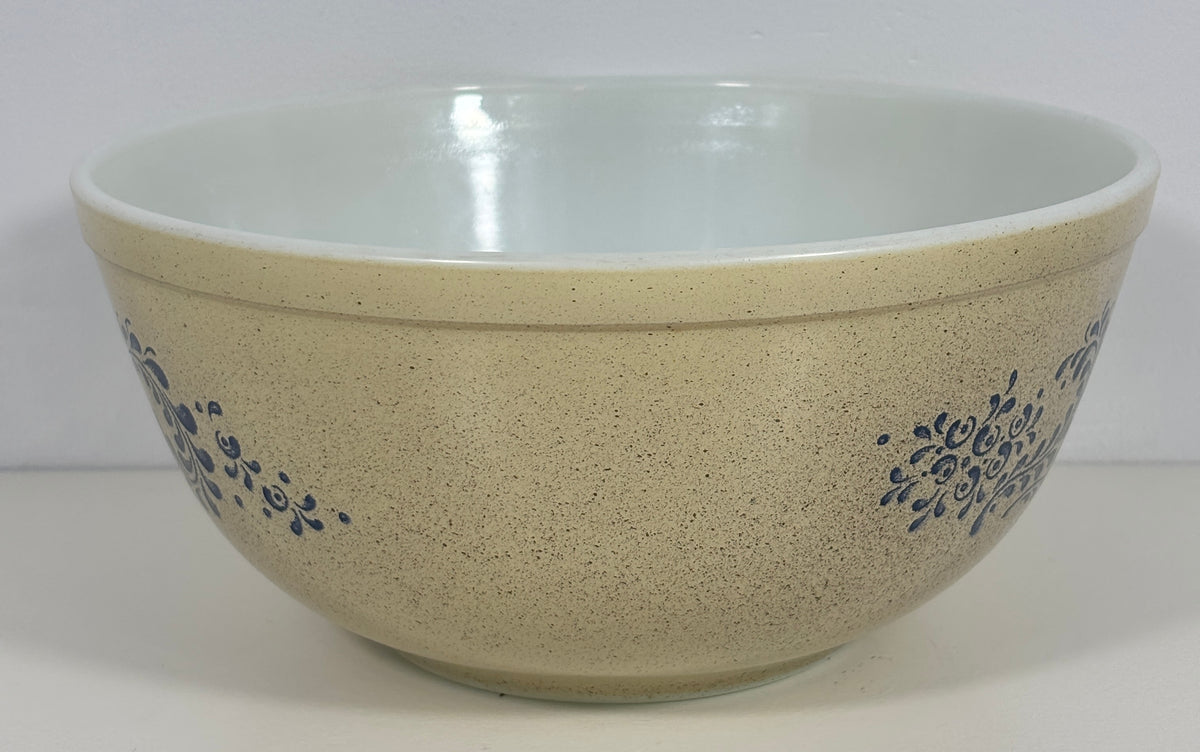 A speckled beige mixing bowl with a glossy white interior and blue floral scroll patterns on the sides, set against a plain white background.