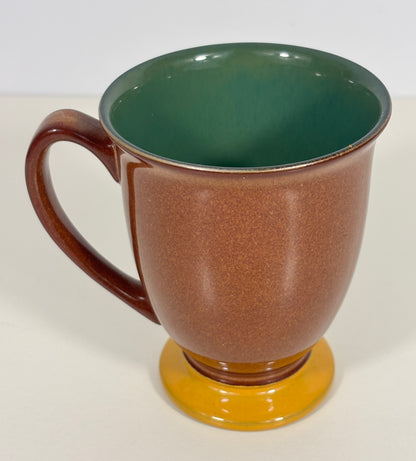 A ceramic mug with a textured brown exterior, a glossy dark green interior, and a round mustard yellow base, shown on a plain light background.