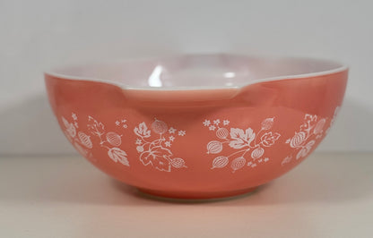 A coral pink Pyrex mixing bowl with a white floral pattern, photographed against a neutral light gray background.