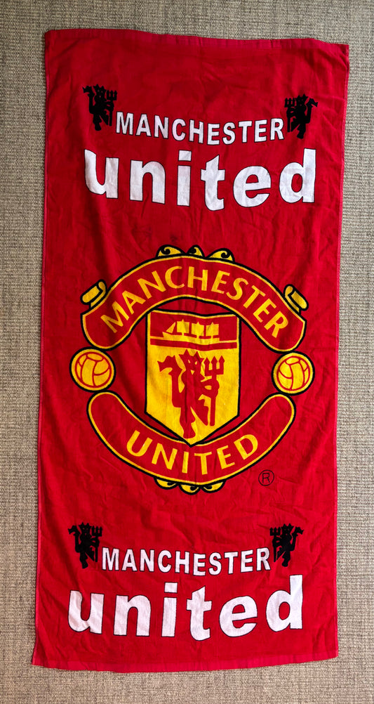 Red Manchester United towel with logo and text on a textured surface