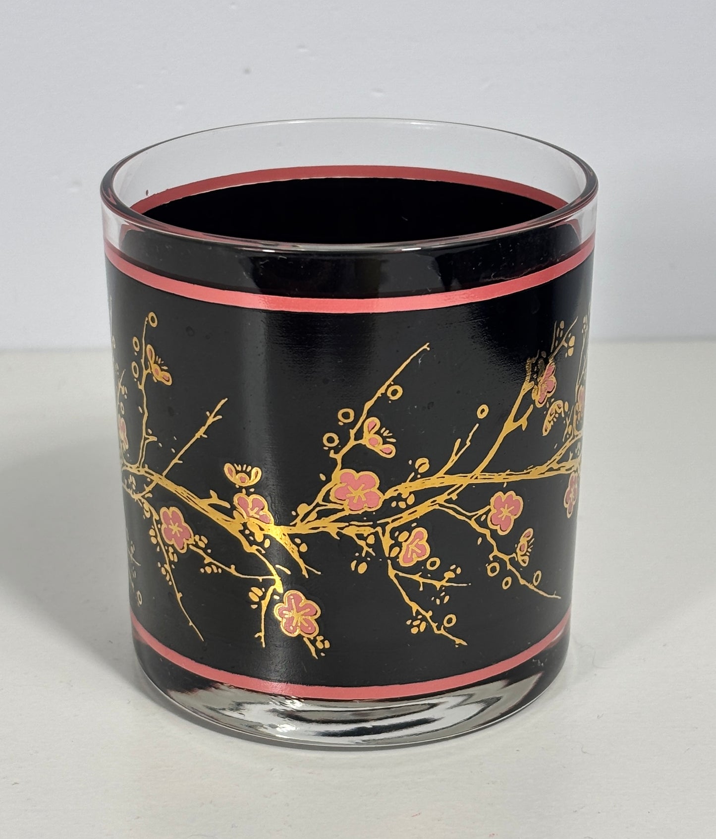 Glass candle holder with black background and gold floral design on a white surface