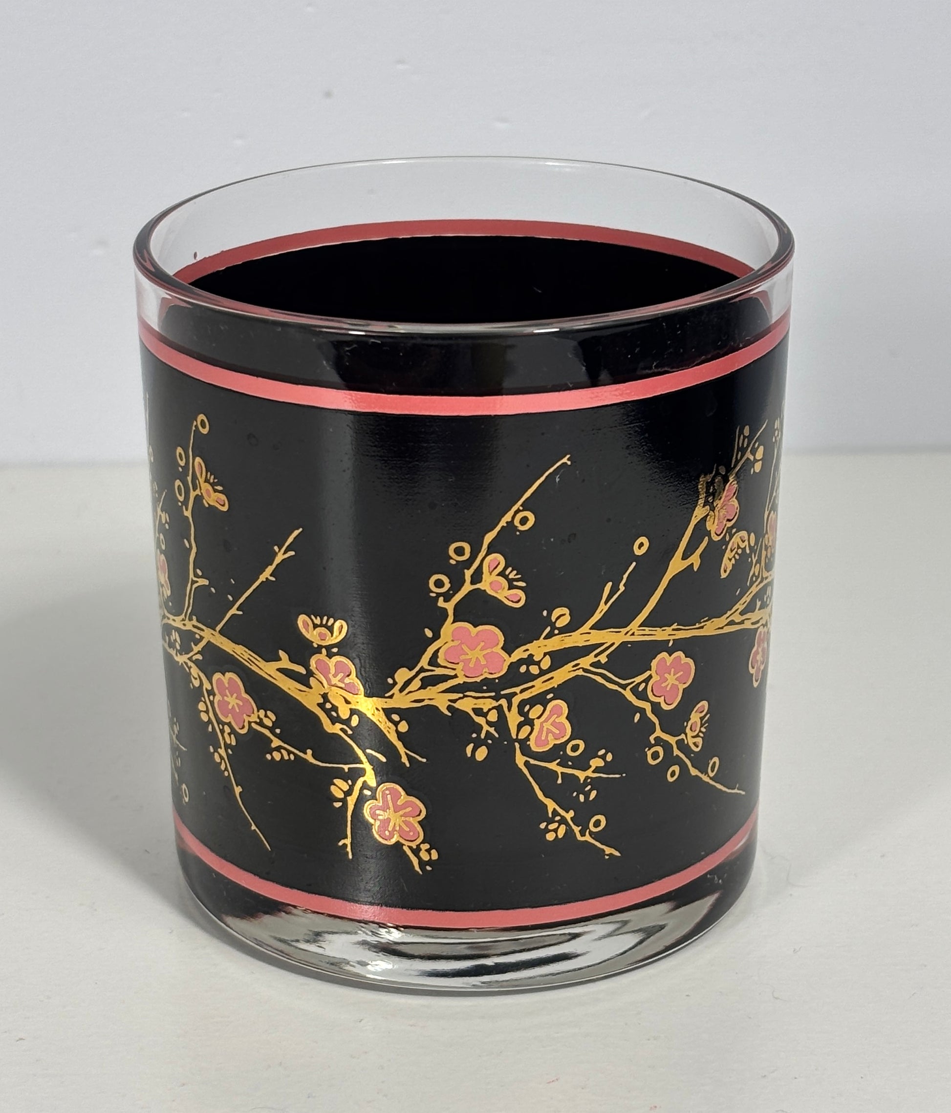 Glass candle holder with black background and gold floral design on a white surface