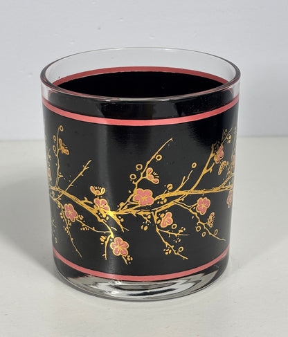 Glass candle holder with black background and gold floral design on a white surface