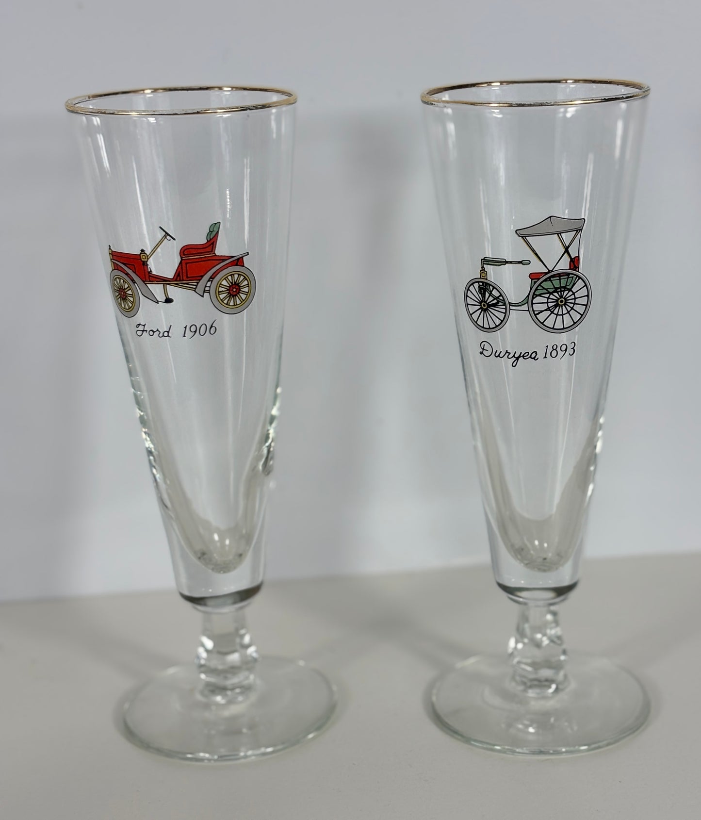 Two glass tumblers with vintage vehicle illustrations on a plain background