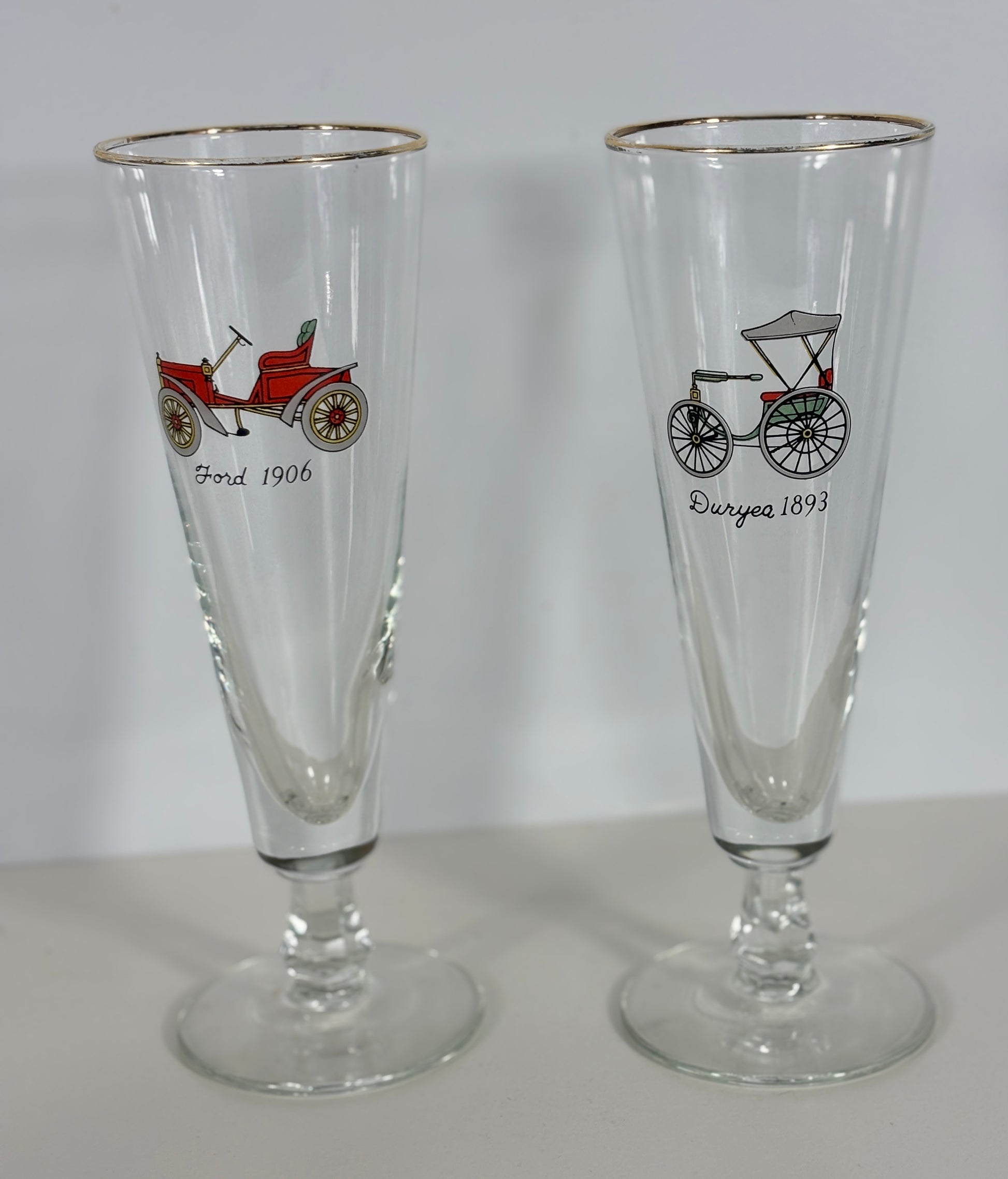 Two glass tumblers with vintage vehicle illustrations on a plain background