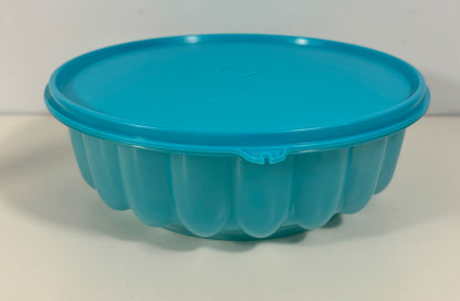 A bright turquoise blue round plastic baking pan with a matching lid, featuring a fluted bottom, shown on a plain white background.