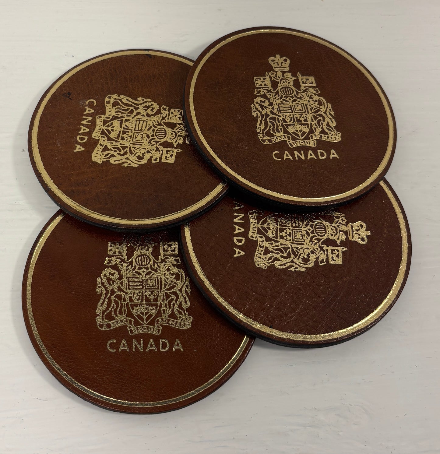 Four brown leather coasters with 'Canada' and a crest design on a white background