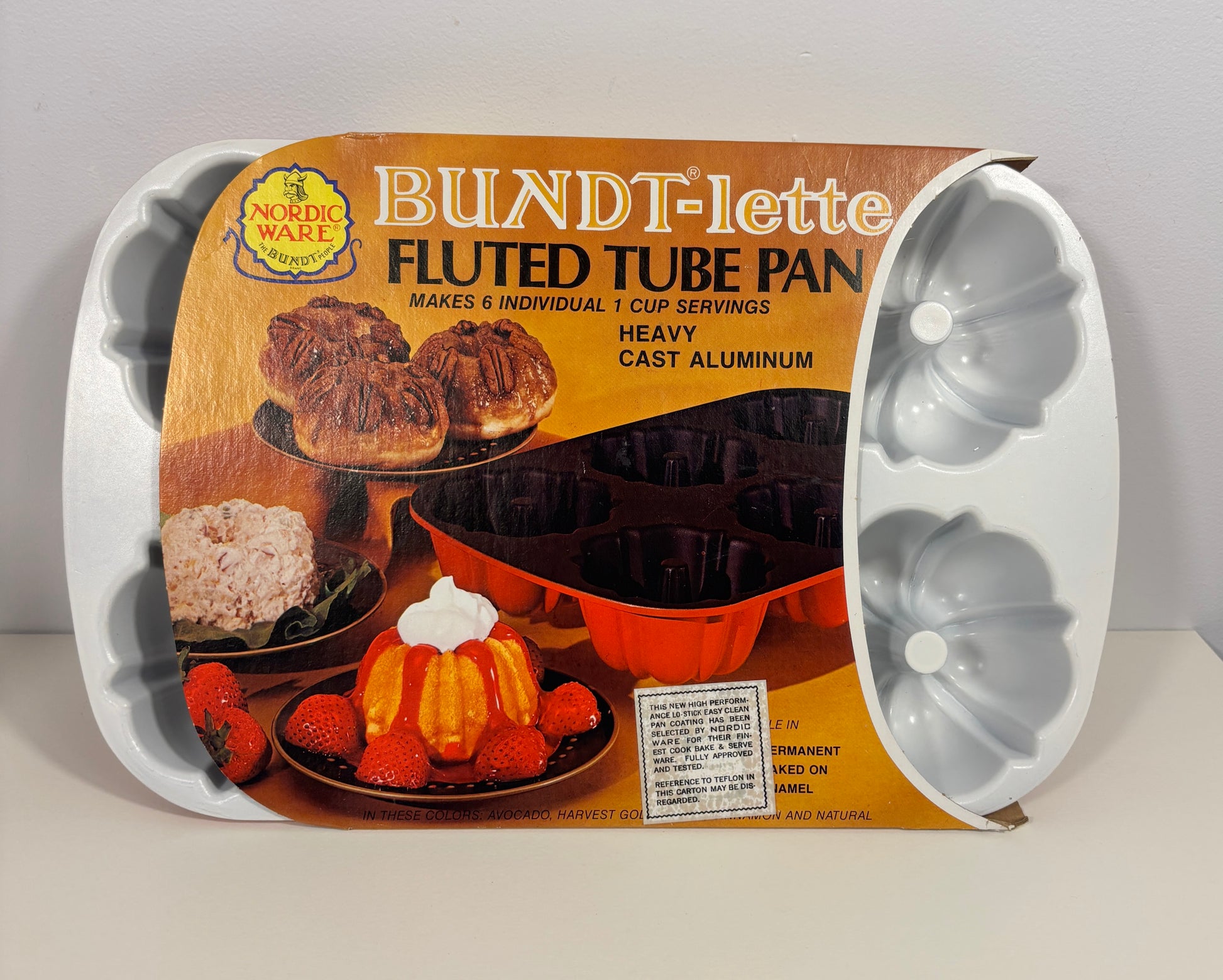 Nordic Ware Bundt-Lette fluted tube pan in its original retail packaging, showing the white cast aluminum fluted mold on the right and the printed cardboard insert on the left.
