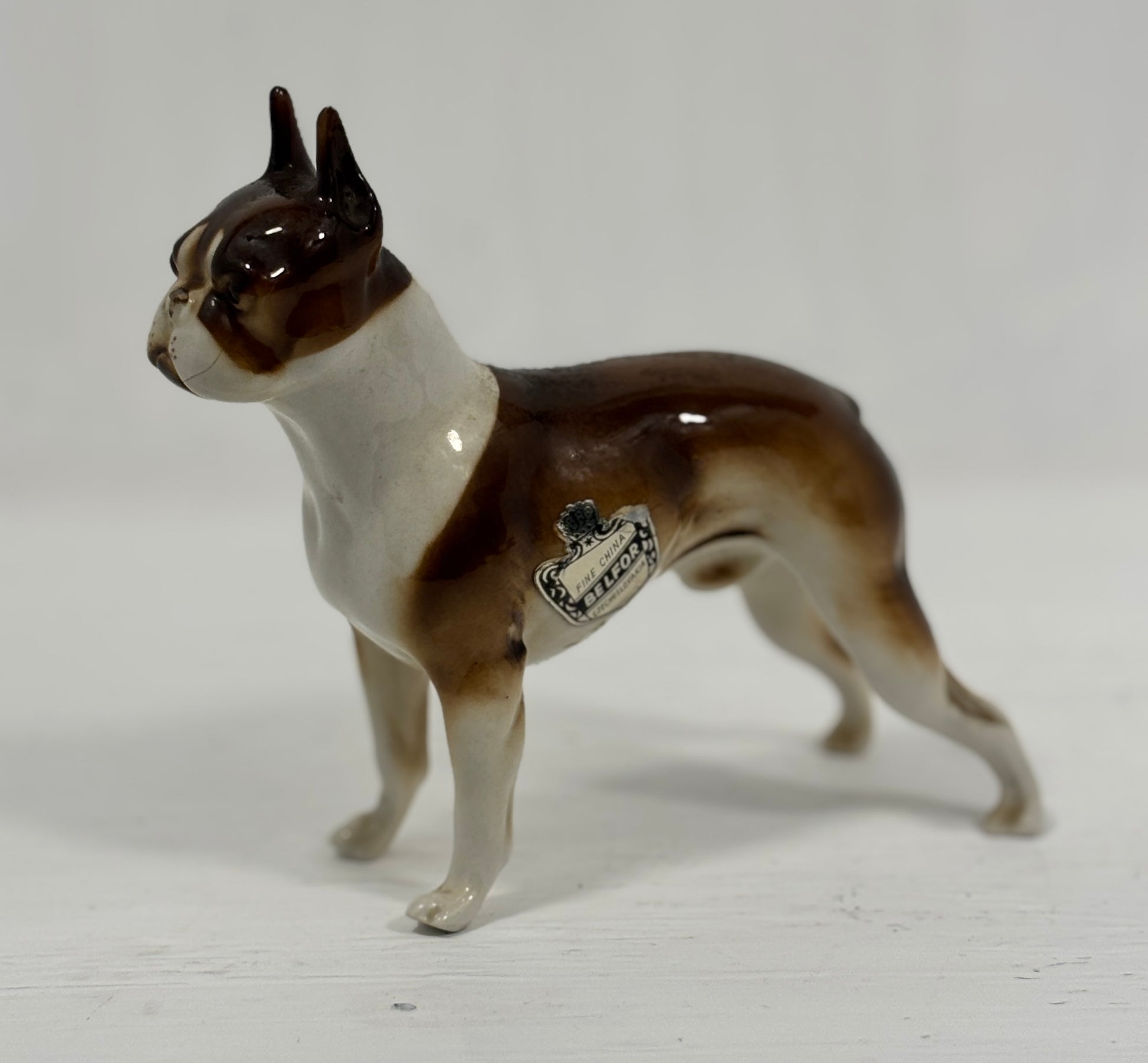 Porcelain figurine of a dog with a white and brown color pattern on a light gray background