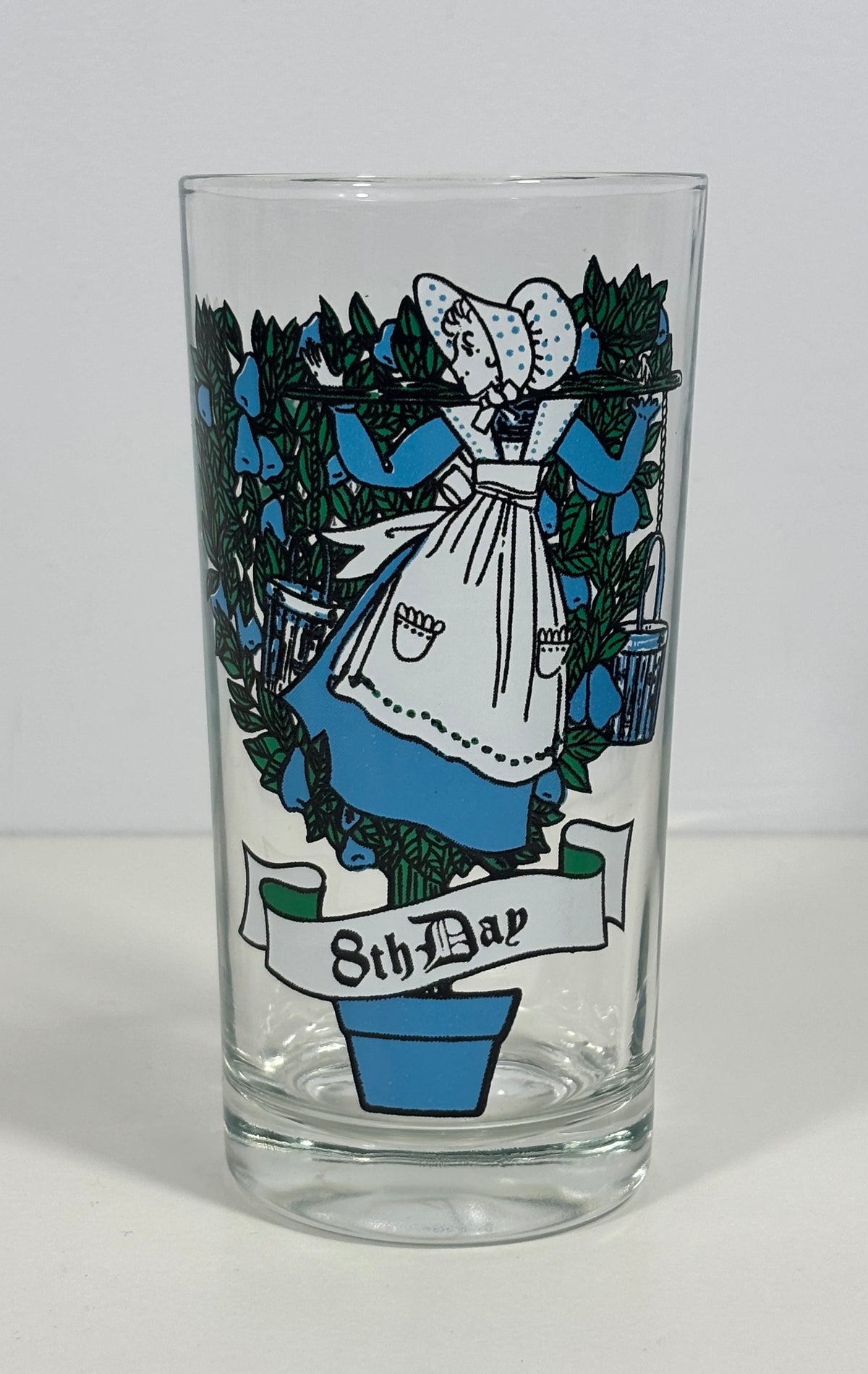 A clear glass tumbler featuring a vintage-style illustration of a woman in a white bonnet and blue dress among green leaves, with a banner reading '8th Dad' at the bottom, shown on a plain light background.