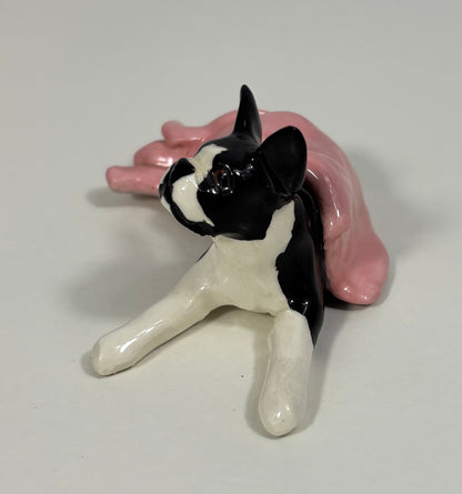 Ceramic figurine of a black and white dog on a pink cushion with a white background