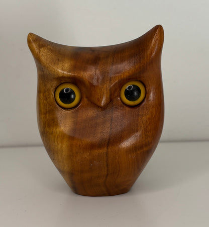 Wooden owl figurine with yellow eyes on a plain background