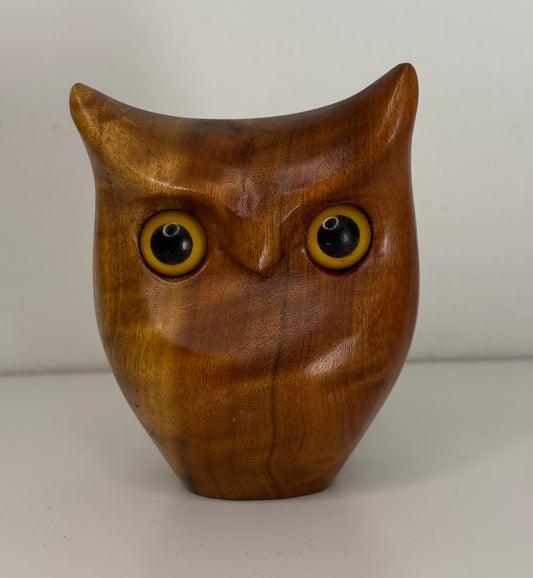 Wooden owl figurine with yellow eyes on a plain background