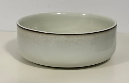 A round ceramic bowl with a speckled off-white glaze and a thin dark rim, photographed against a plain light background.