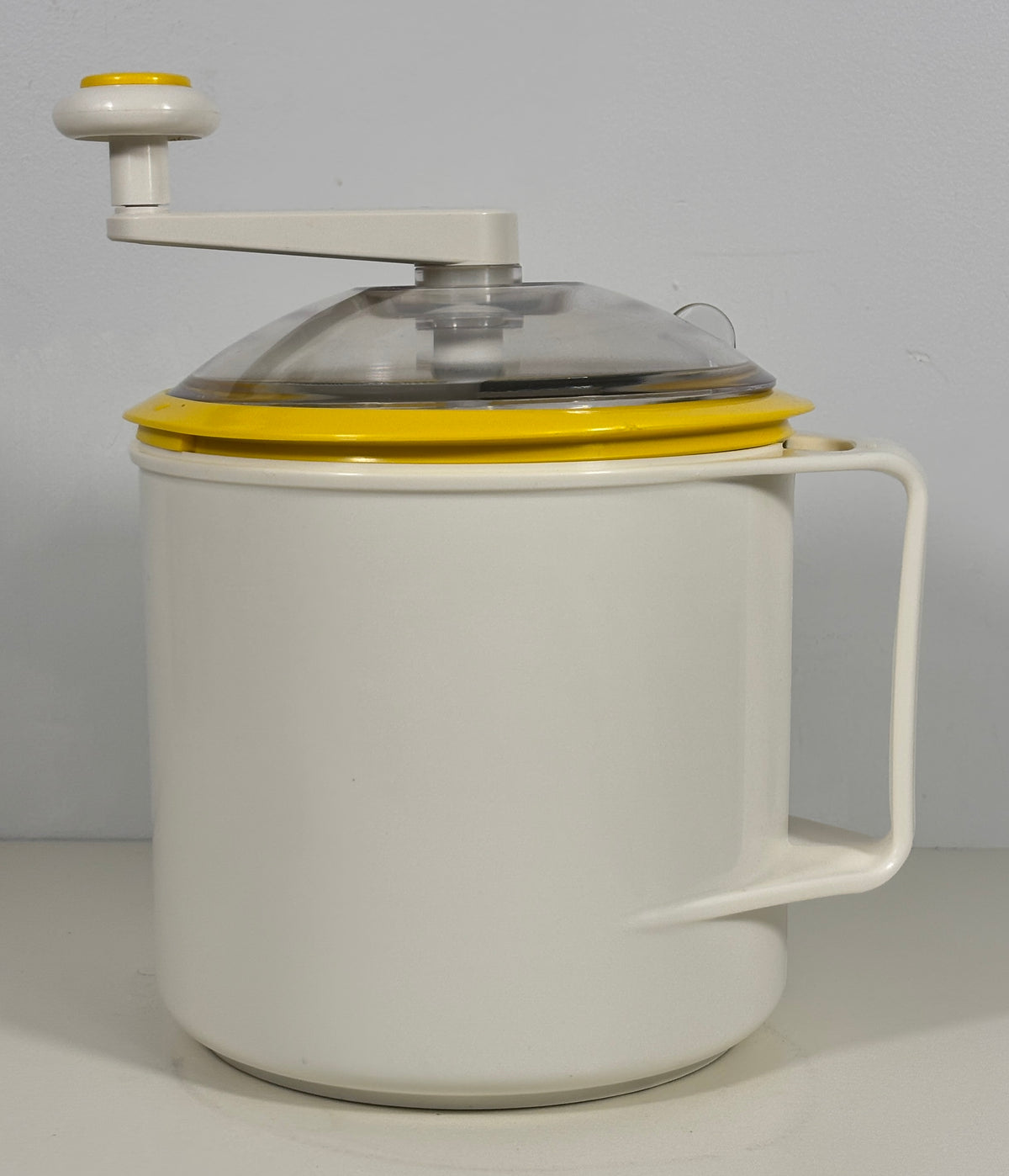 A vintage-style hand-crank ice cream maker with a white body, yellow accents, and a clear lid, shown against a plain light gray background.