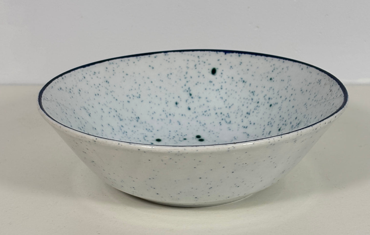 A white ceramic bowl with dark green speckles and a dark blue rim, shown against a plain light gray background.