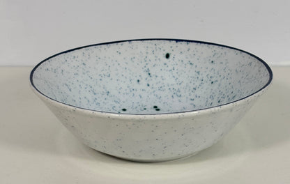 A white ceramic bowl with dark green speckles and a dark blue rim, shown against a plain light gray background.