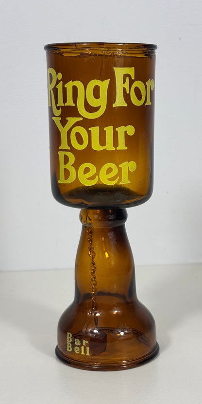 An amber glass goblet with a wide base, featuring the phrase 'Ring For Your Beer' printed in yellow on the front and 'Bar Bell' near the bottom, set against a plain white background.