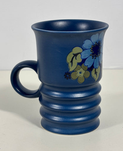 A cobalt blue ceramic mug with a ribbed base and a floral pattern featuring blue, yellow, and green flowers, set against a plain light background.