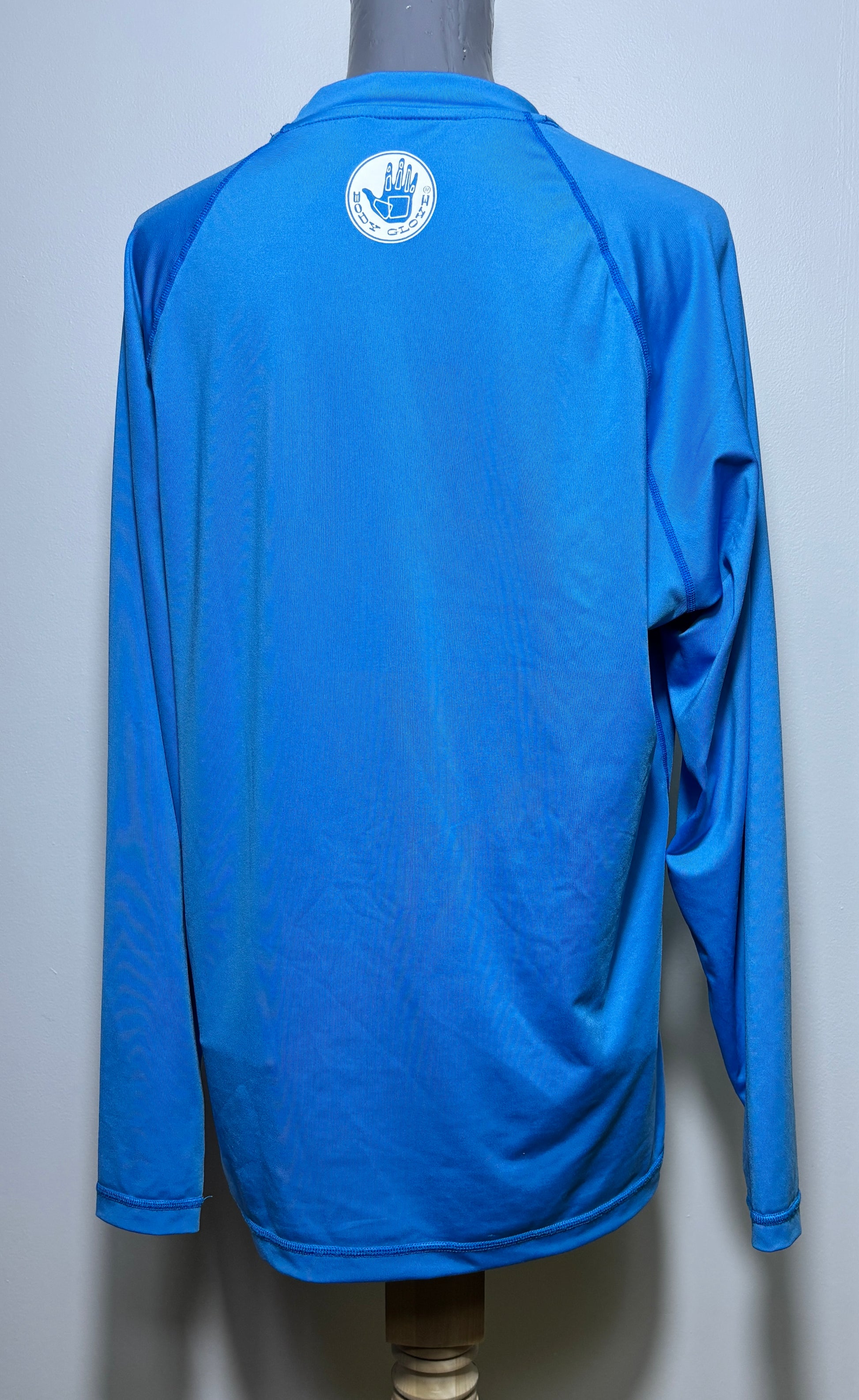 Blue long-sleeve shirt with a logo on the back, displayed on a mannequin against a light gray background.