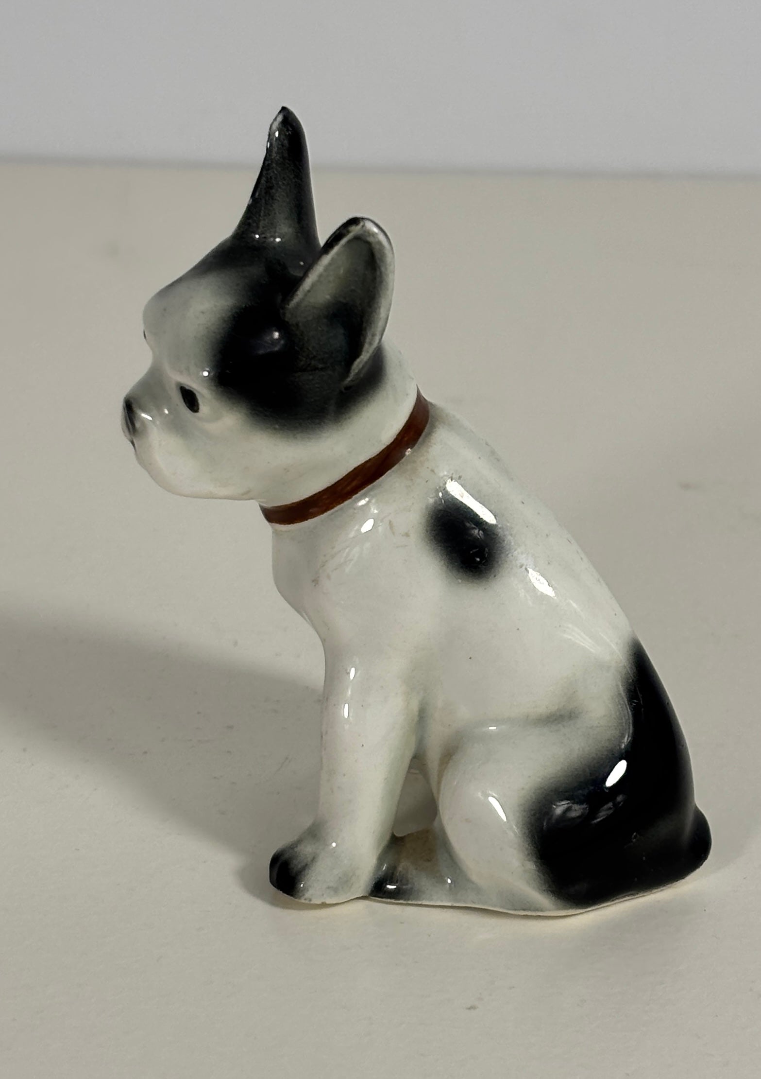 Small ceramic figurine of a dog with black and white markings on a plain background