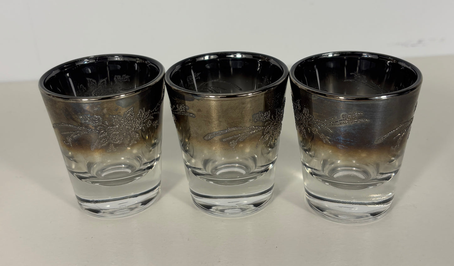 Three silver-rimmed shot glasses on a white surface