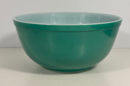 A classic green glass mixing bowl with a light blue interior, photographed against a neutral off-white background.