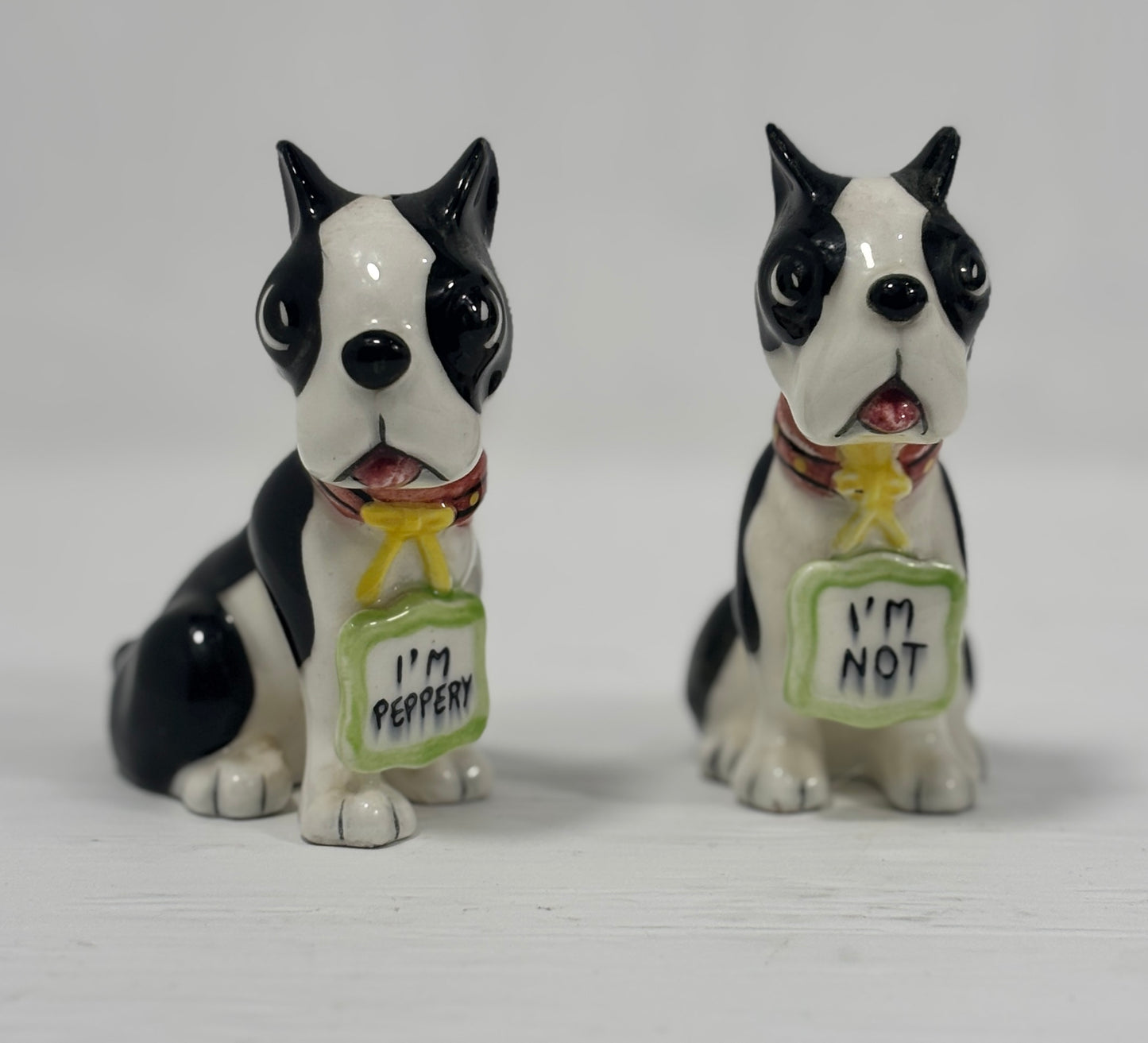 Two black and white dog figurines with 'I'm Pepper' and 'I'm Not' signs on a white background