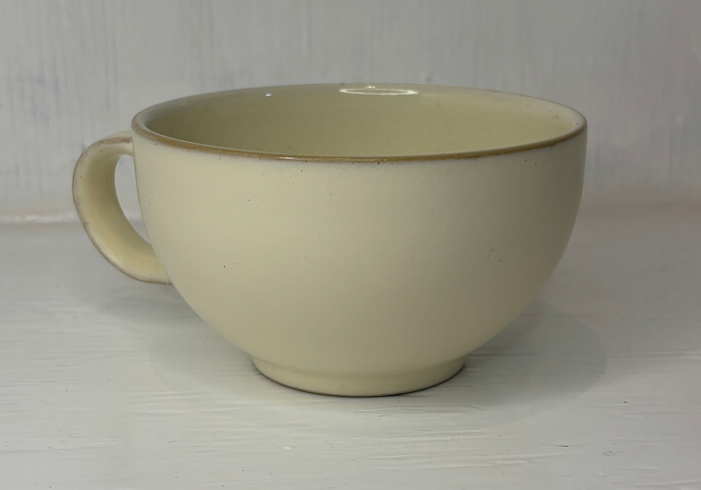 Beige ceramic mug with a brown rim on a white background