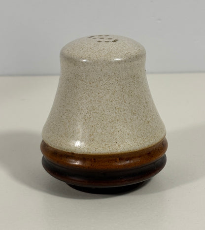 A small ceramic shaker or container with a conical beige speckled glaze top and a dark brown glazed base, photographed on a plain light background.