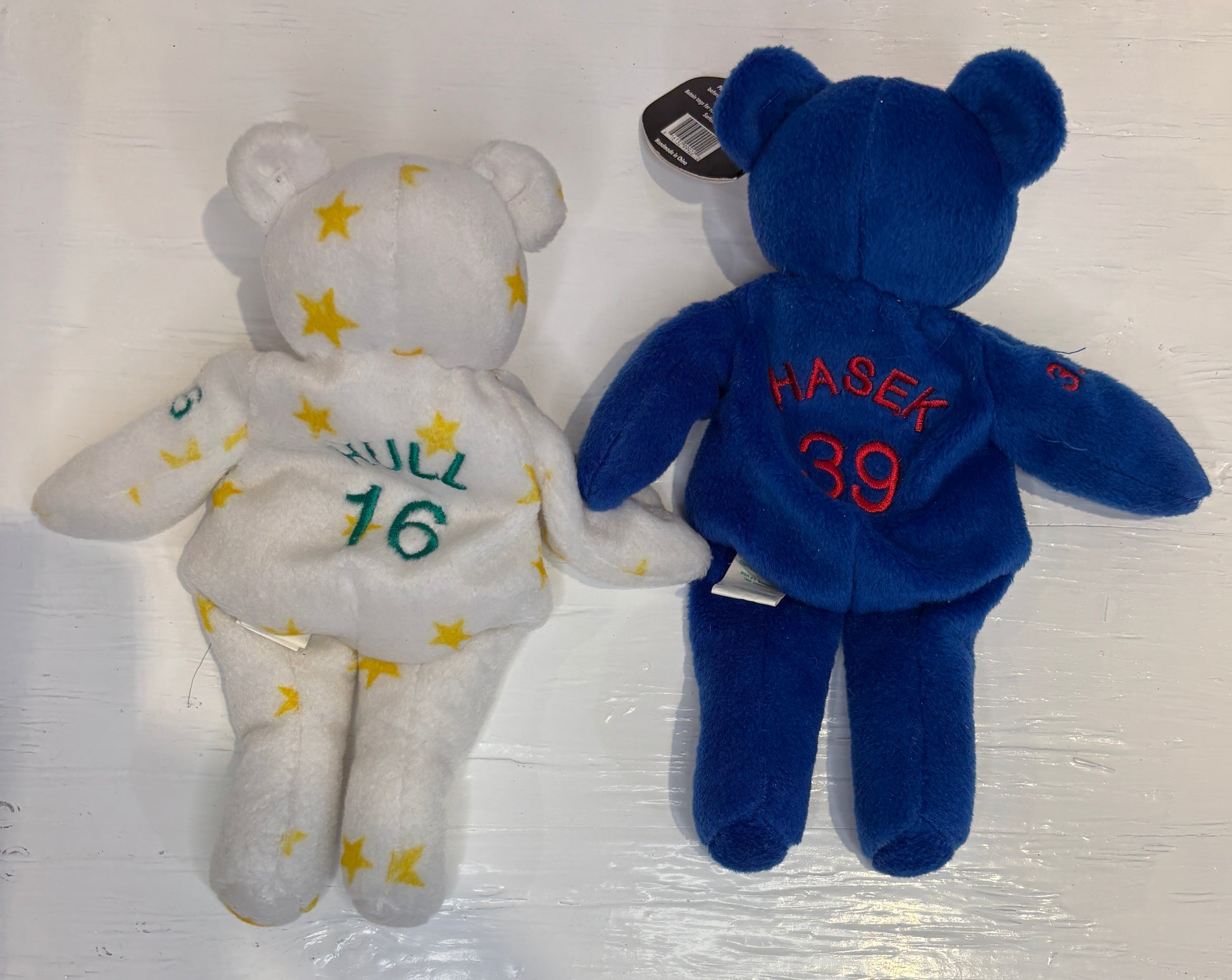 Two teddy bears, one white with yellow stars and green text, the other blue with red text, on a light background.