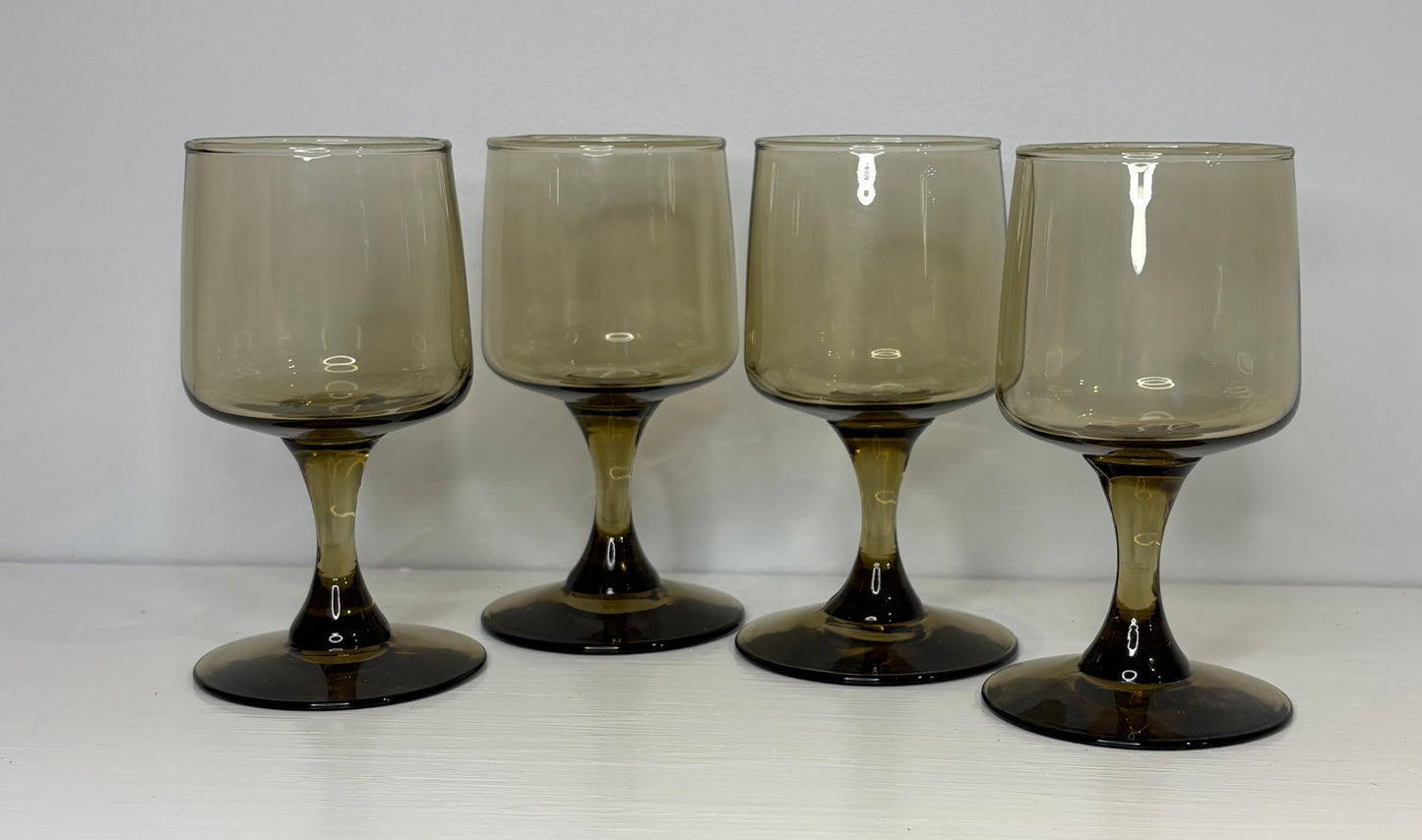 Four smoked glass goblets on a white surface with a light gray background