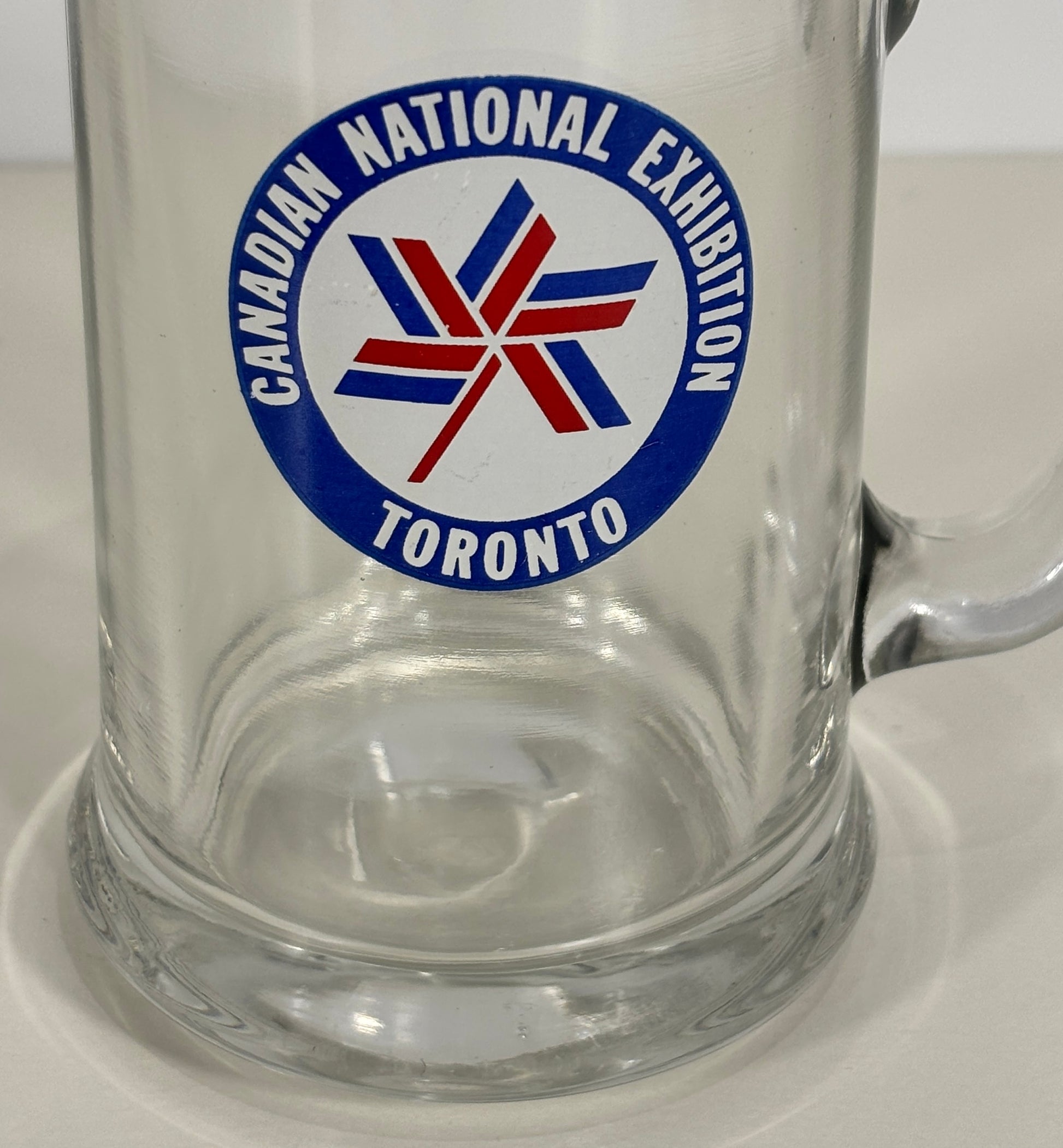 Clear glass mug with Canadian National Exhibition logo on a white background