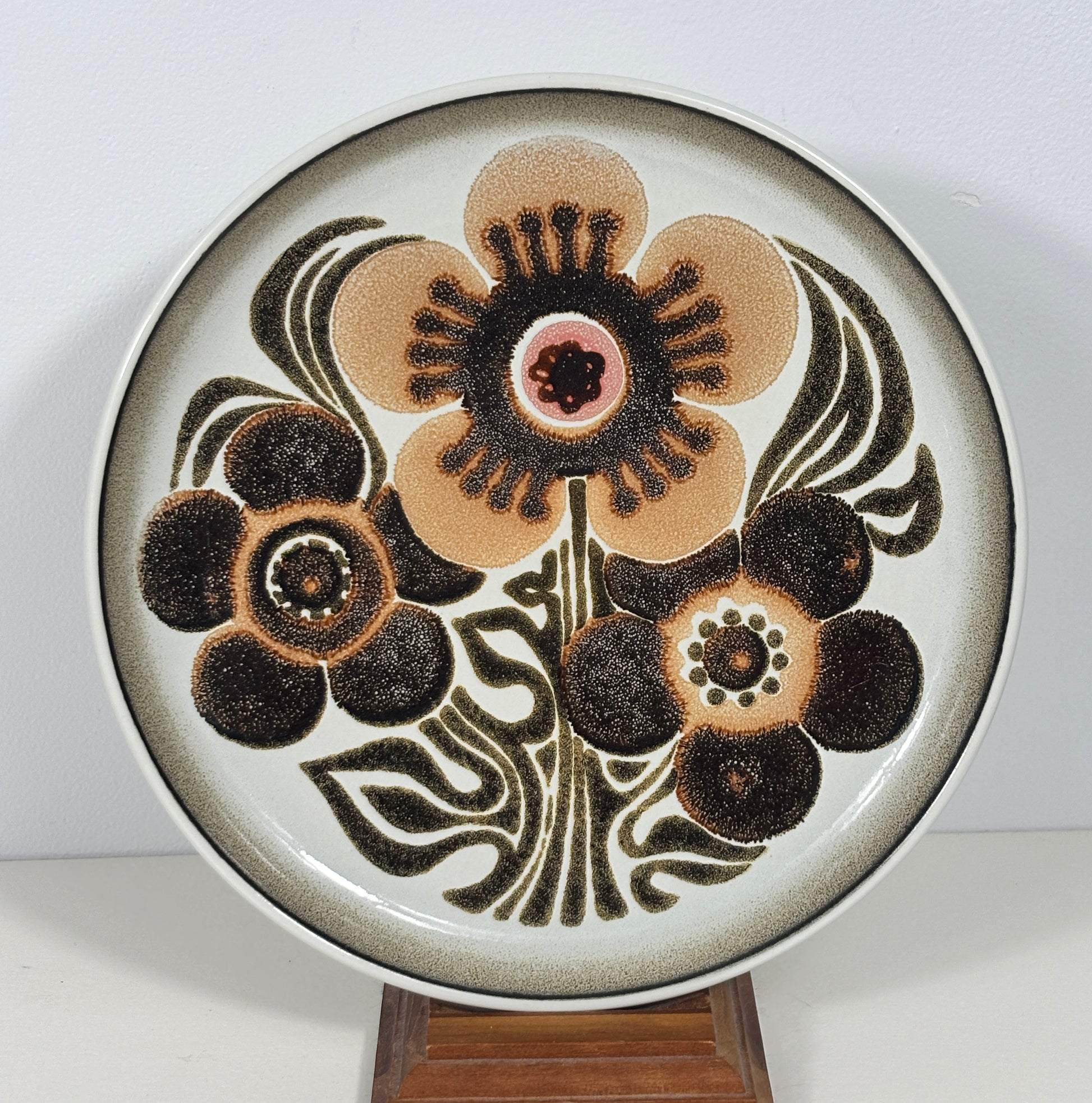 A round ceramic decorative plate with a mid-century modern floral design, displayed on a small wooden stand against a plain white background.