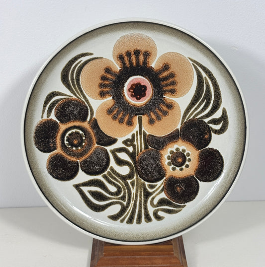 A round ceramic decorative plate with a mid-century modern floral design, displayed on a small wooden stand against a plain white background.