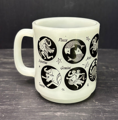 White mug with black astrological signs on a dark surface