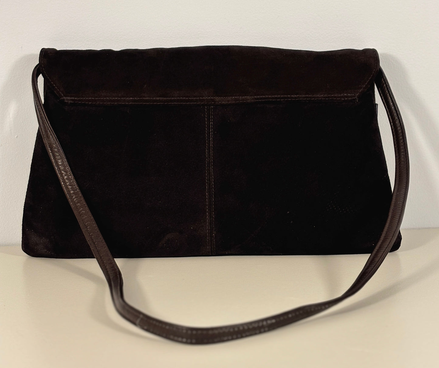 brown suede handbag on a light beige surface with a white background