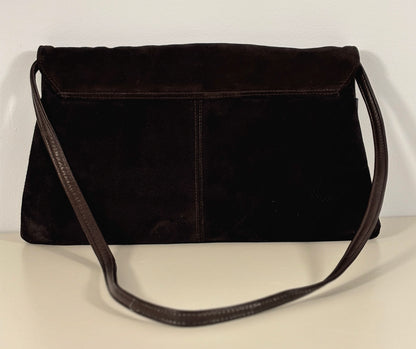 brown suede handbag on a light beige surface with a white background