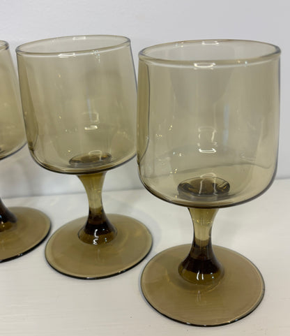 Set of four smoked glass goblets on a white surface with a light gray background
