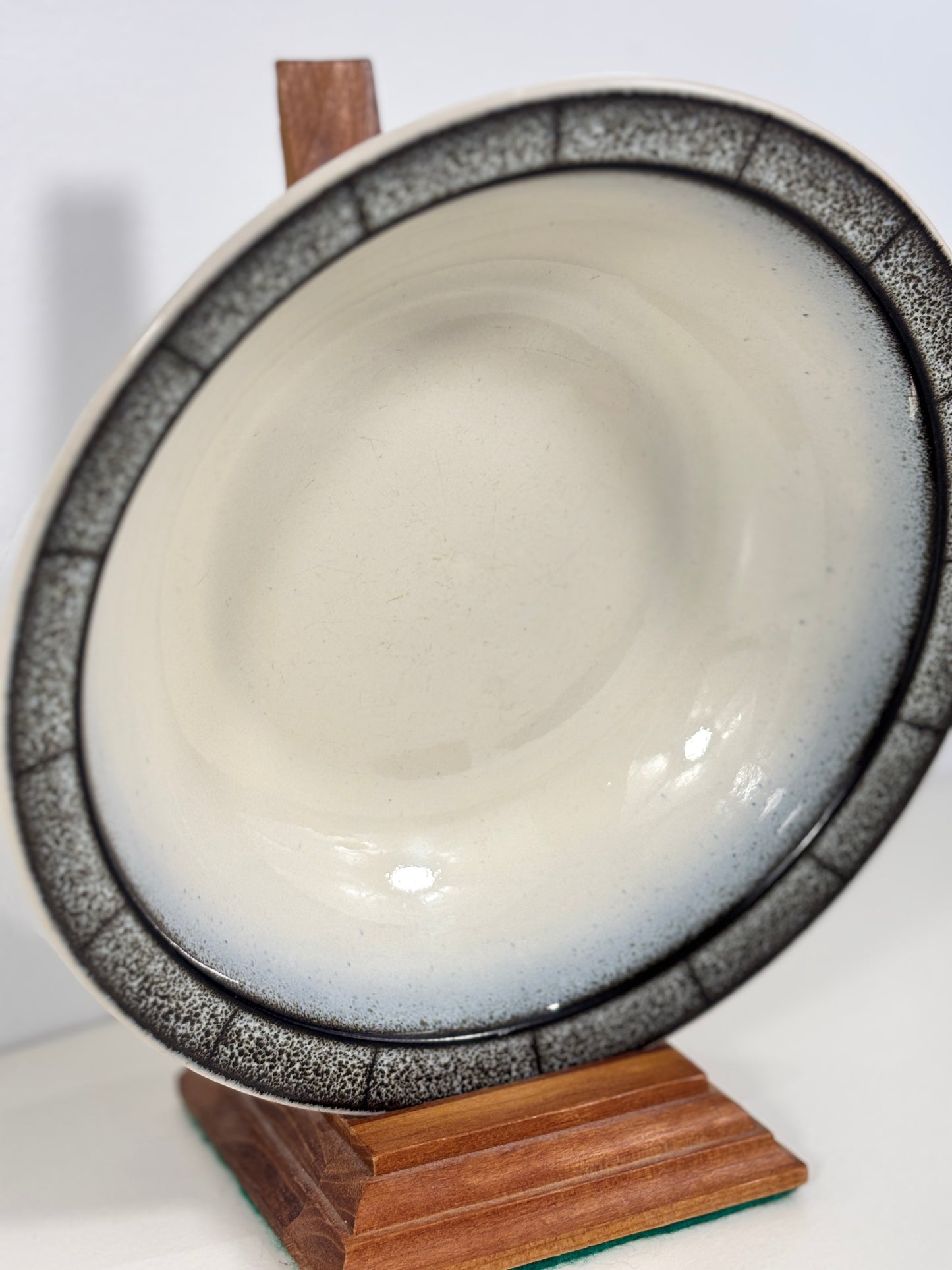 Ceramic bowl with speckled design on a wooden stand against a white background