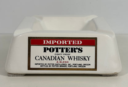 A white ceramic potter's ashtray featuring a vintage-style label that reads 'IMPORTED POTTER'S CANADIAN WHISKY'.
