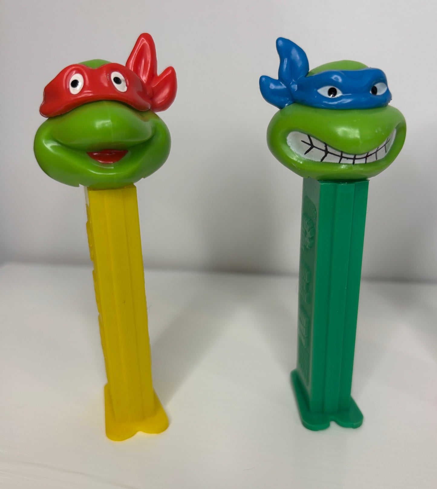 Two PEZ dispensers shaped like turtles with masks on a white background